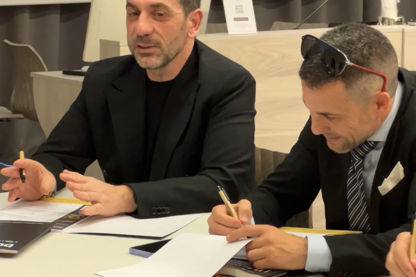 Roberto Chiarolanza at the table with a colleague, Segnalazione Vincente
                      materials open in front of them, during a team-work moment